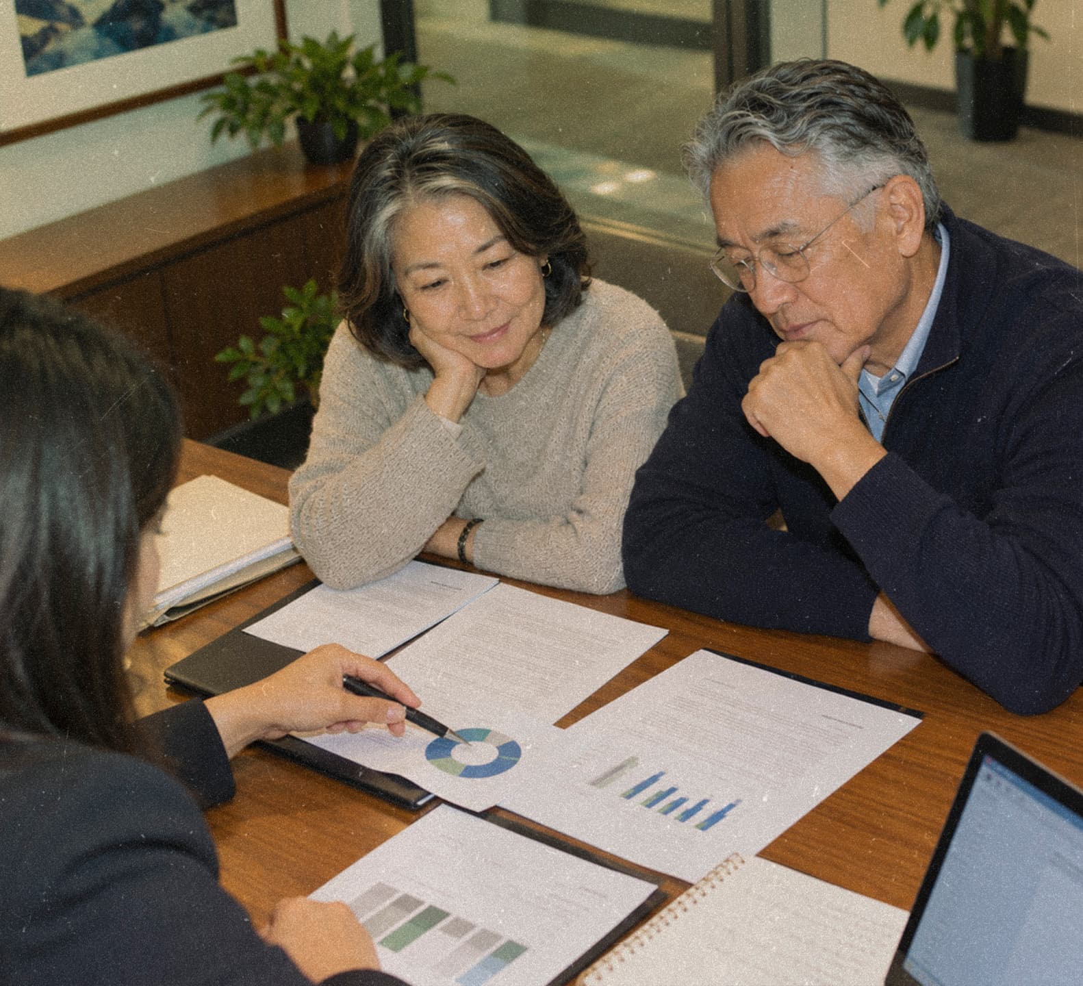 An older couple reviews printed charts with an advisor across a conference table.